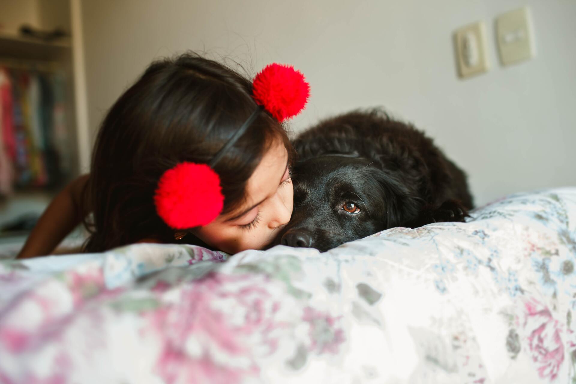 A little girl is laying on a bed with a black dog.