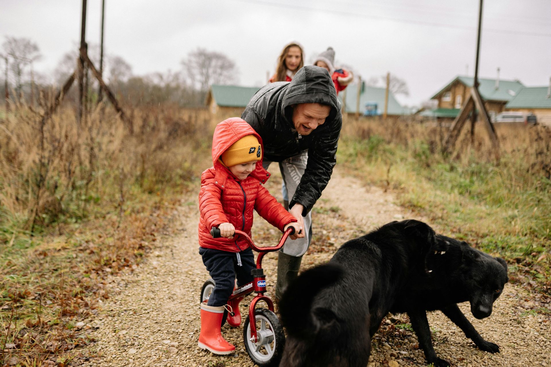 A little boy is riding a bike next to a black dog.