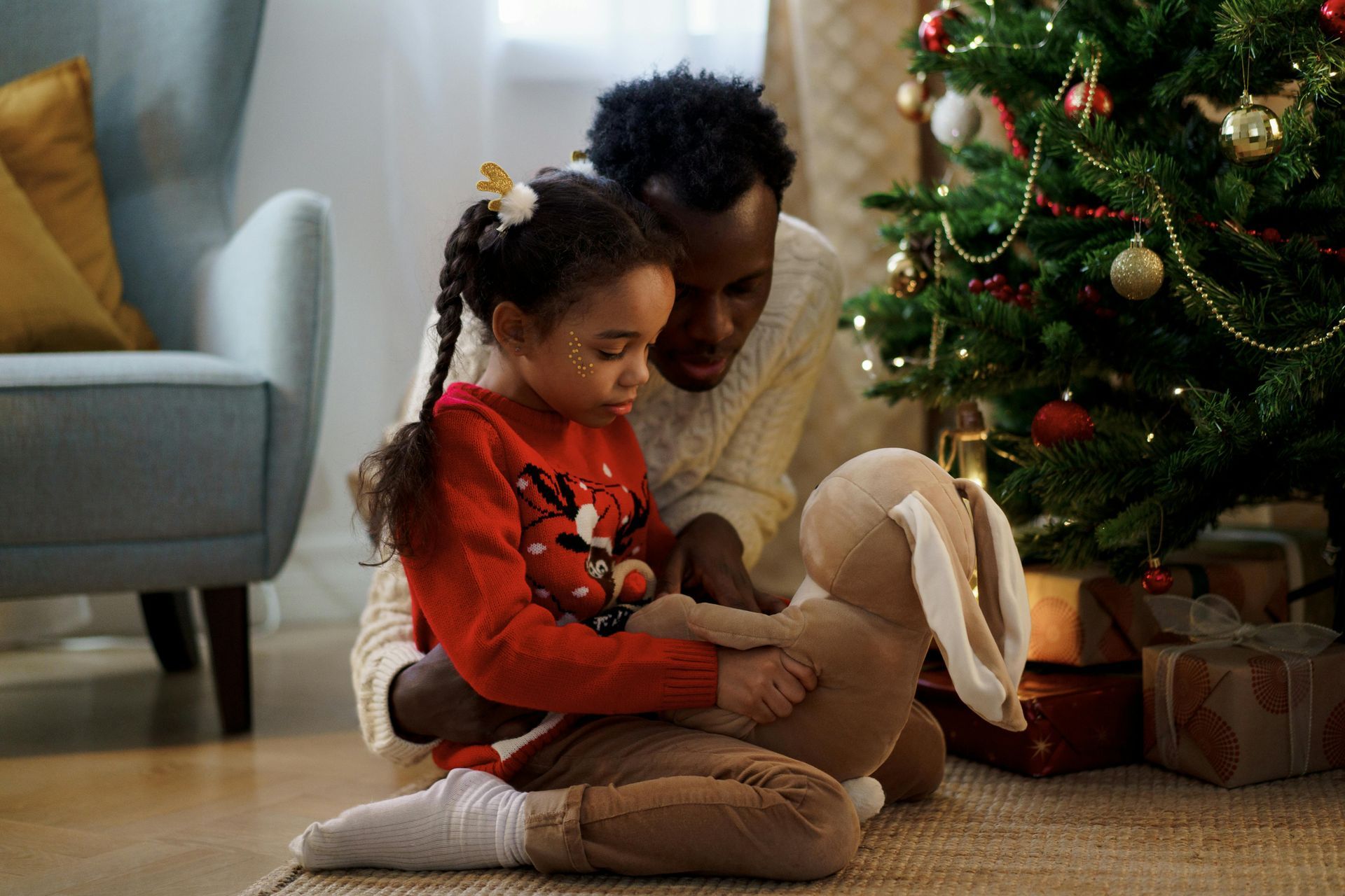 A man and a little girl are sitting on the floor in front of a christmas tree.