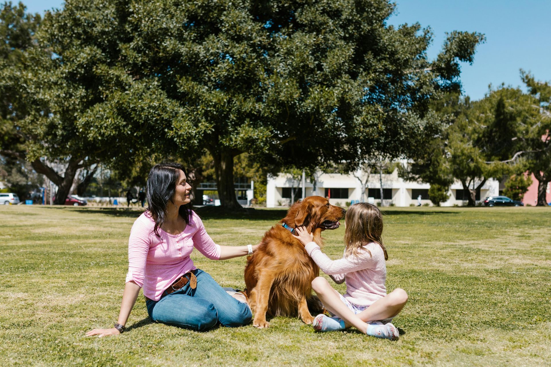 A woman and a little girl are petting a dog in a park.