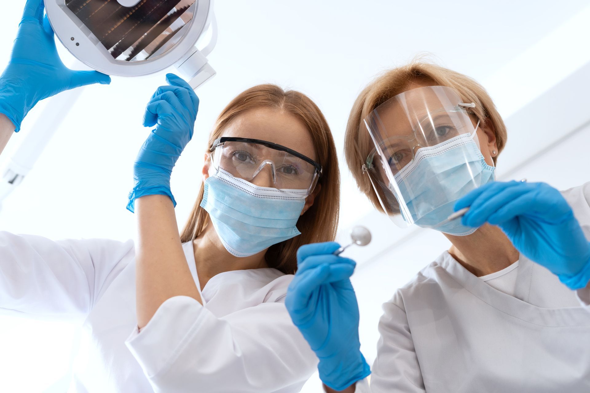Two female dentists wearing masks and gloves are working in a dental office.