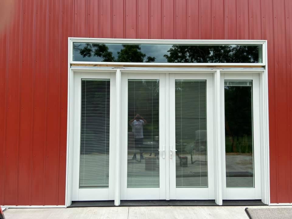 Red building exterior with white-framed glass doors and a transom window, reflecting the outdoors.