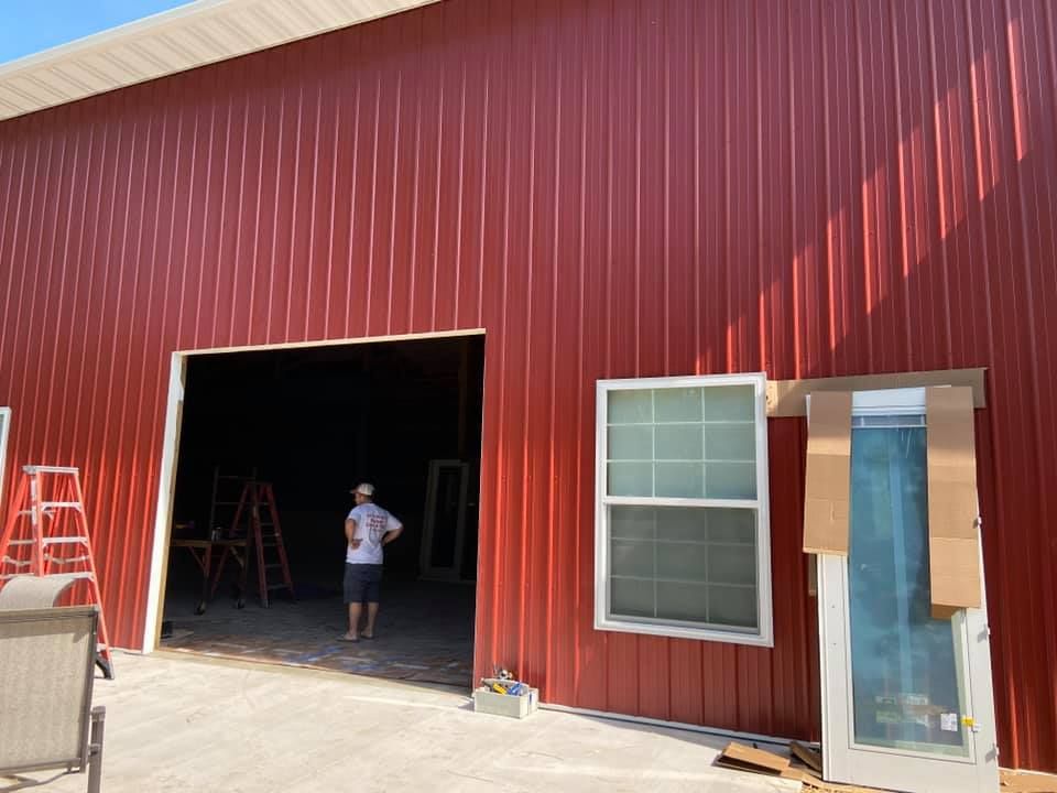 Red metal building with large opening, a man inside, window, and doorway on exterior.