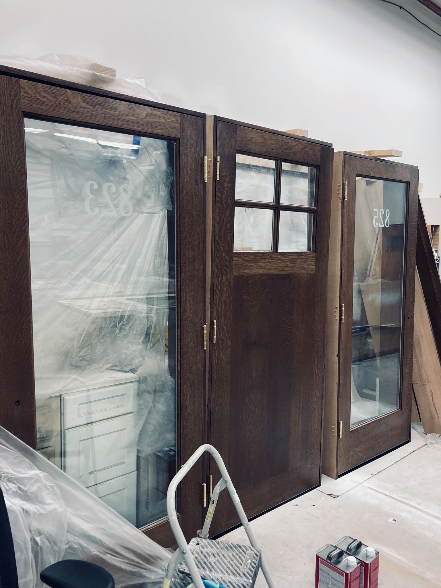 Three wooden doors with glass panels and brown trim, indoors. A stepladder and building materials visible.