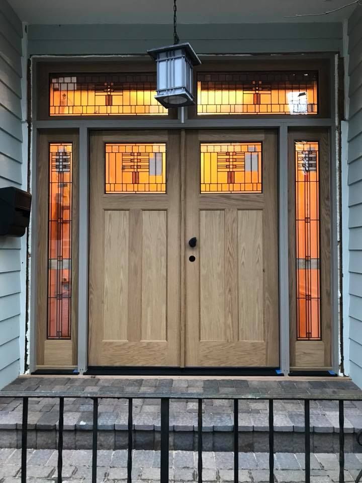 Wooden double front doors with sidelights and transom, lit from within, with a decorative lantern.