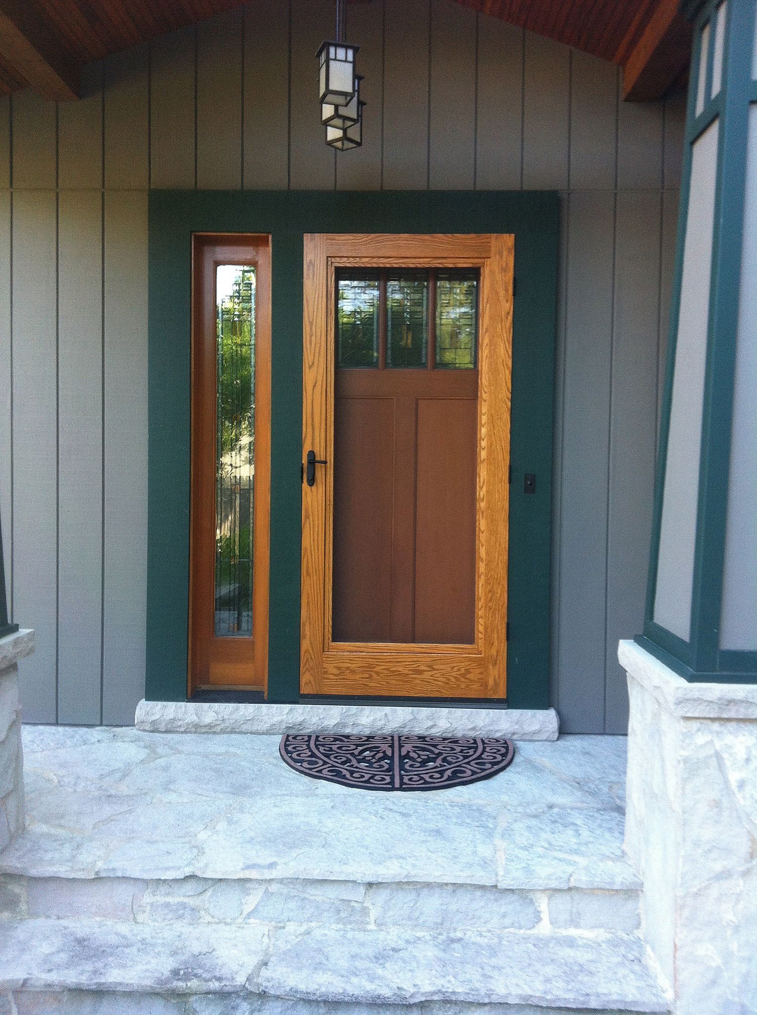 Wooden door with sidelight, framed in green, on a stone porch.