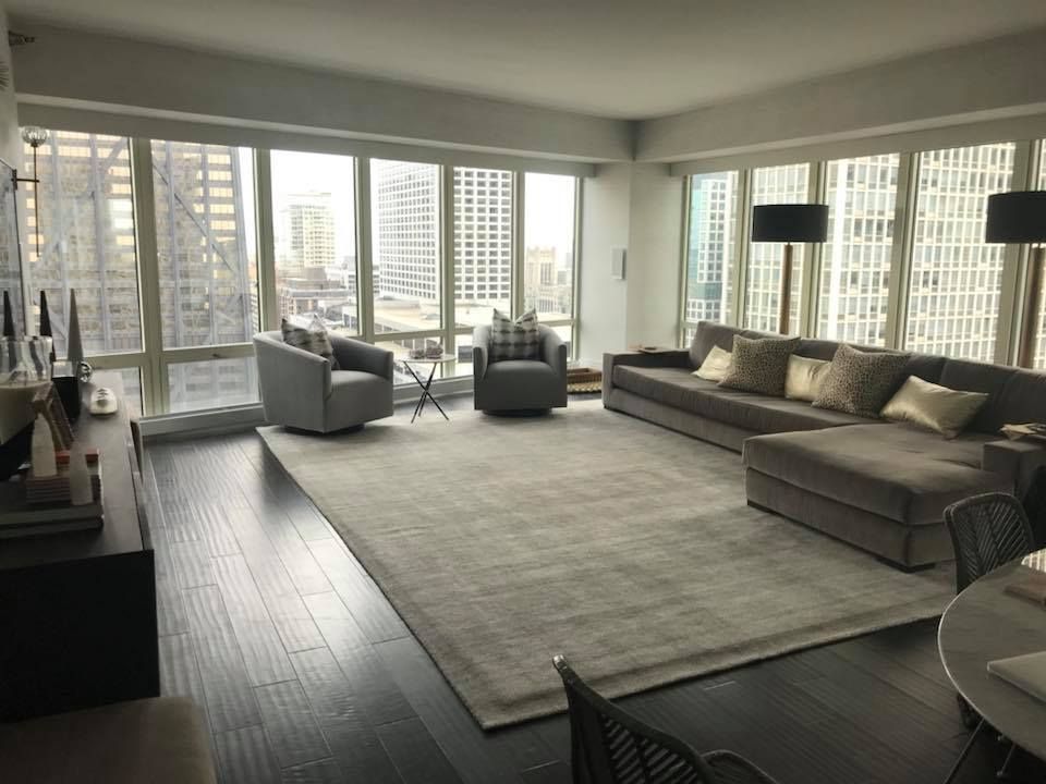 Living room with city views, dark hardwood floors, gray sectional sofa, two armchairs, and large rug.