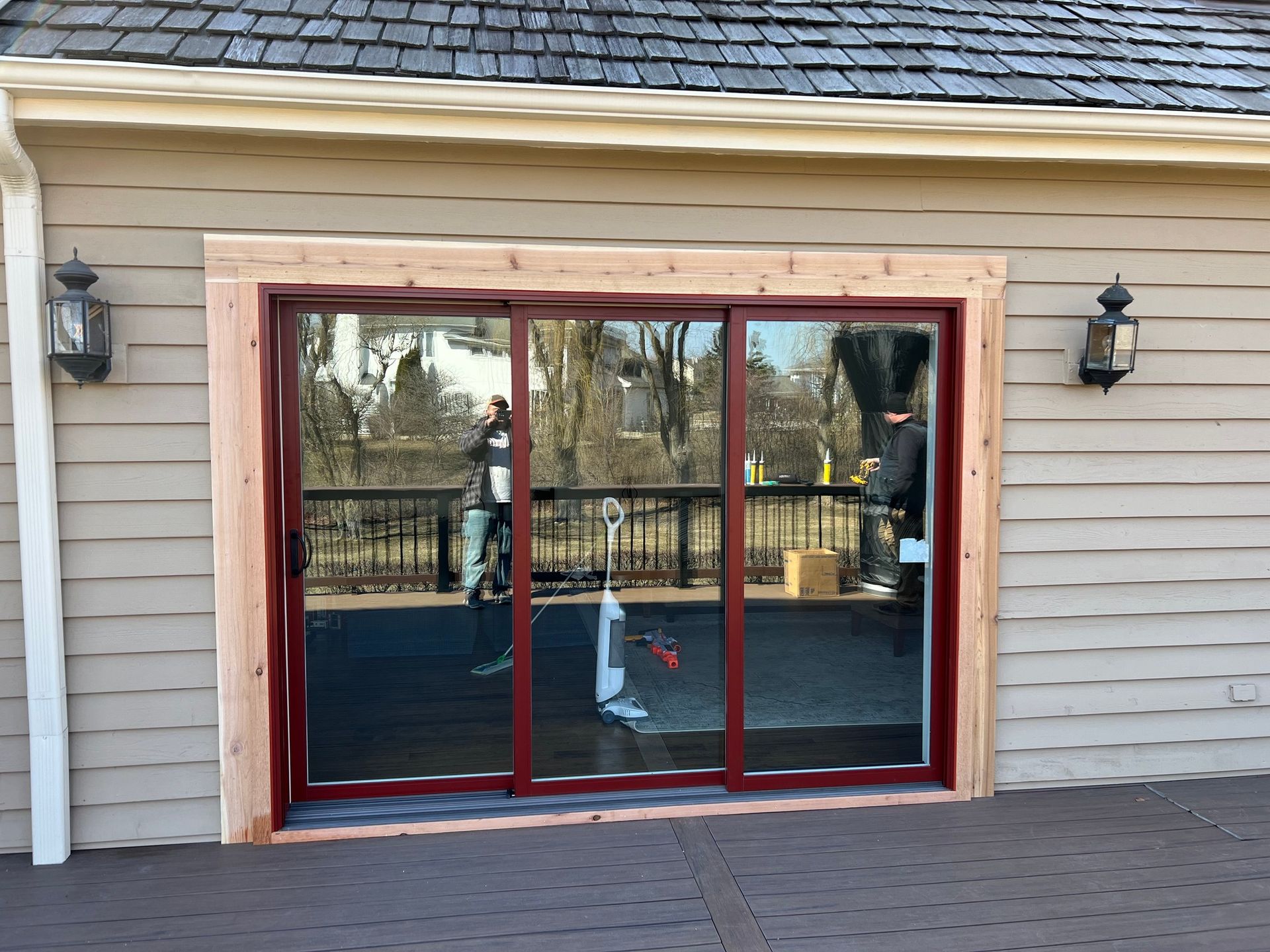 Sliding glass door with red frame and wood trim, set in a wood-sided building. Two sconces are on either side.