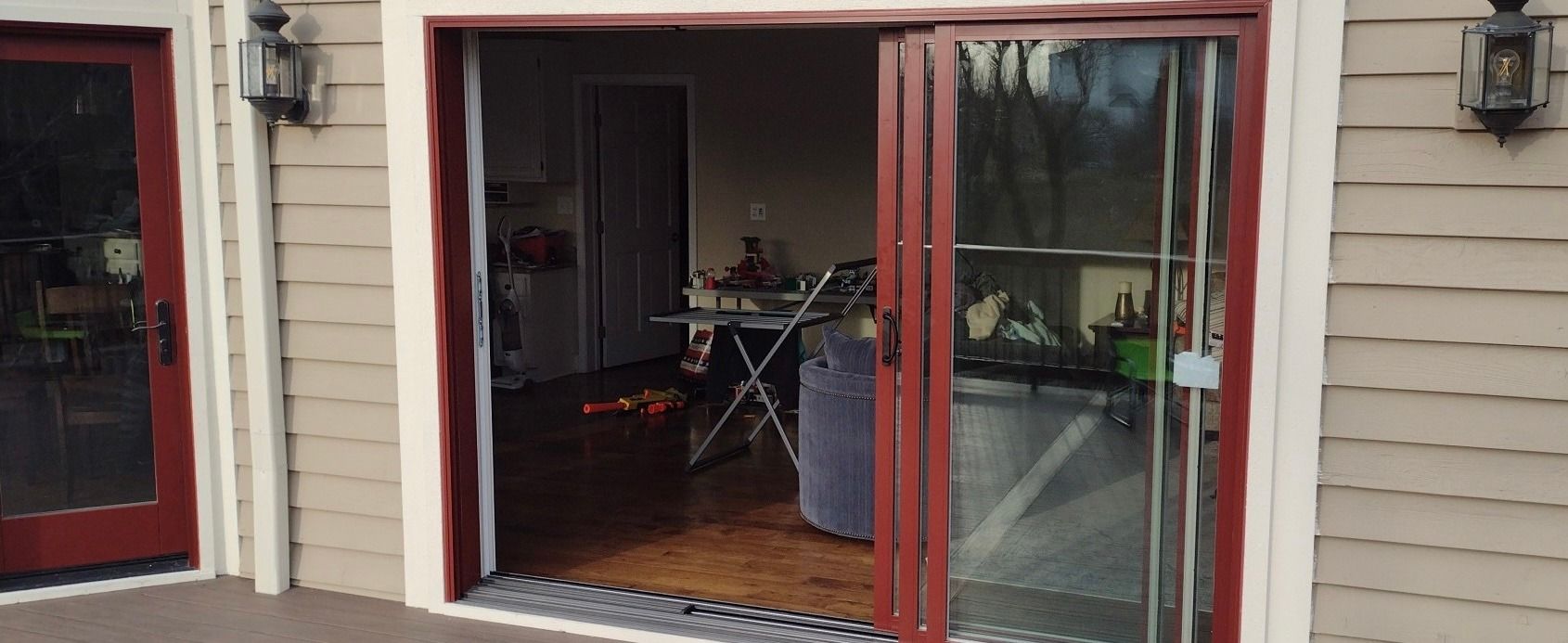 Exterior view of a house with red-framed glass doors and a red door. Beige siding, with interior visible.