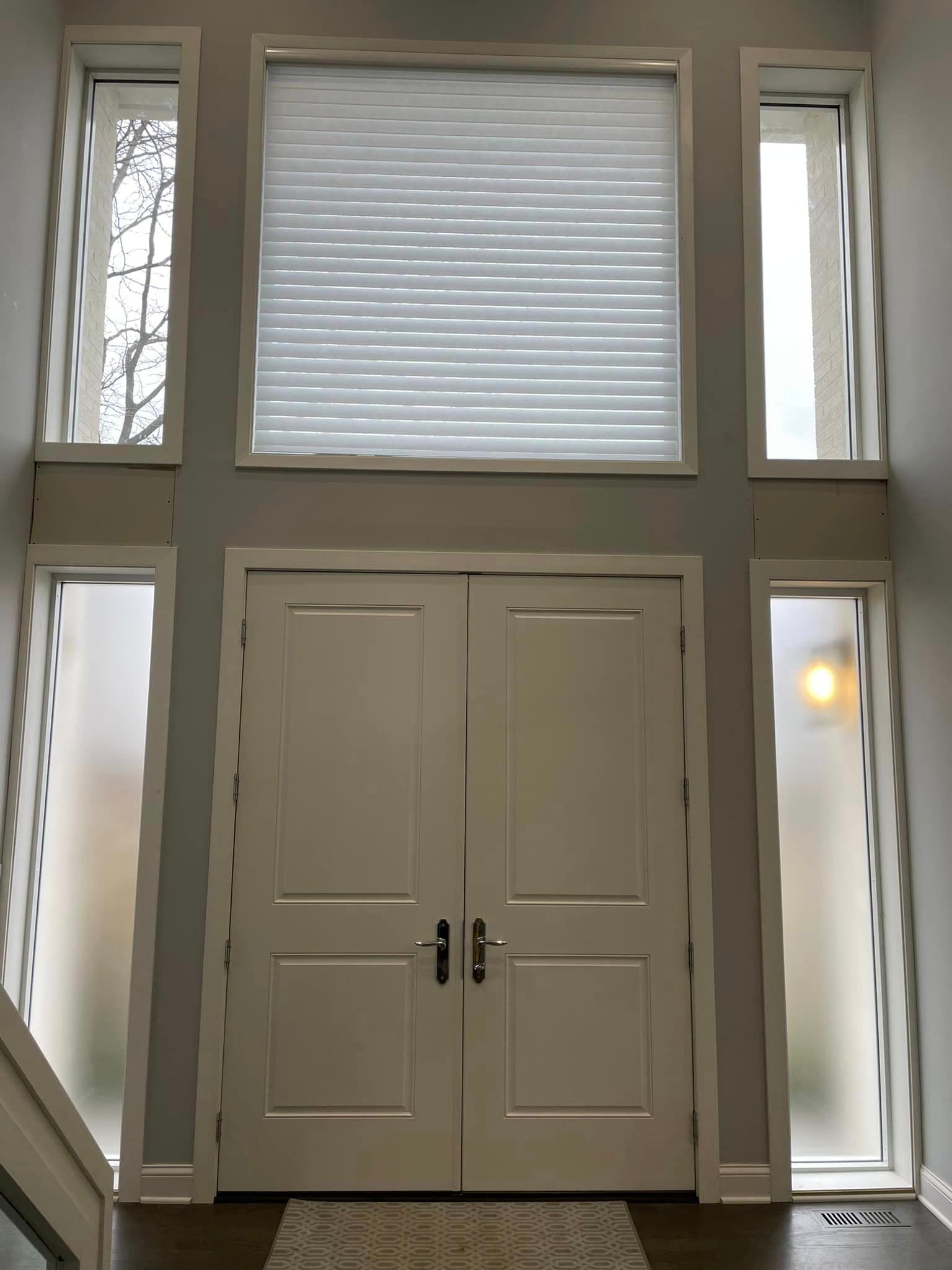 White double doors with sidelights and an upper window, all framed in white, with a frosted appearance in the sidelights.