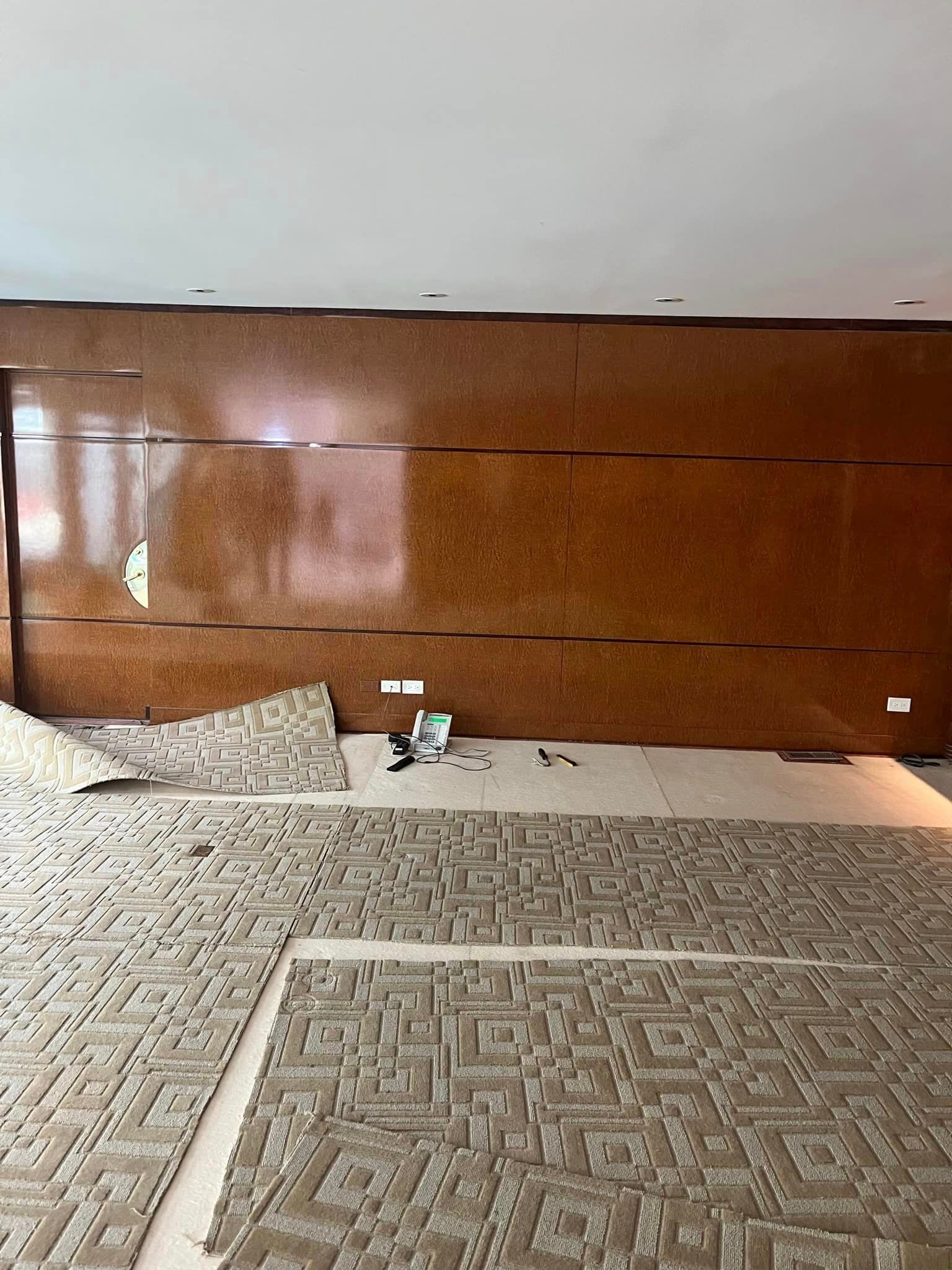 Installation of patterned tile flooring in a room with a brown paneled wall; construction in progress.