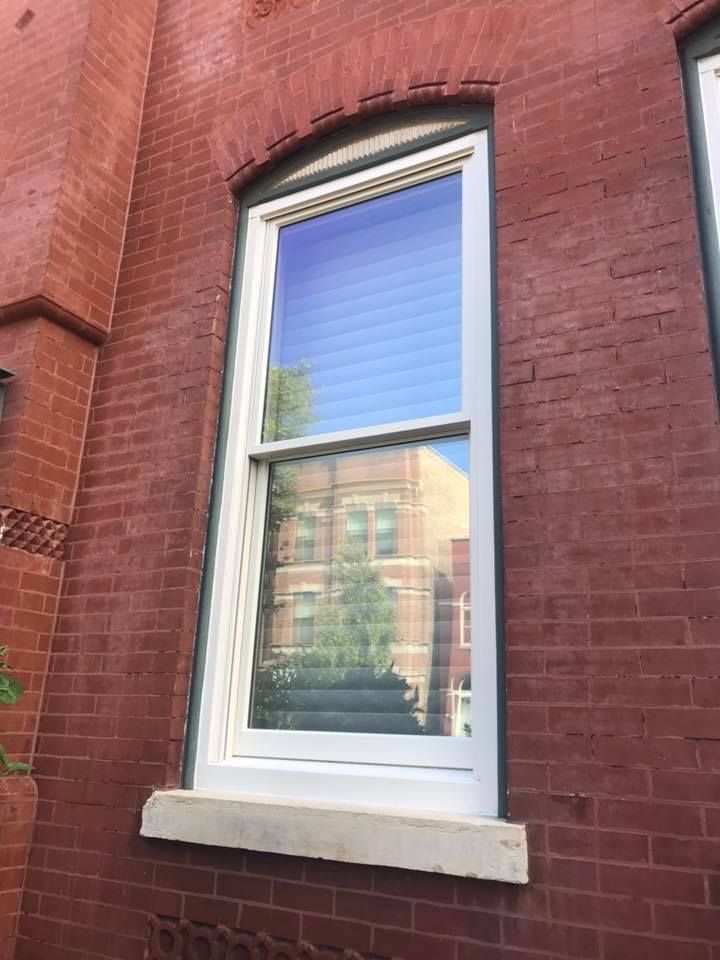 Tall white window in red brick wall; reflection of building visible in glass.