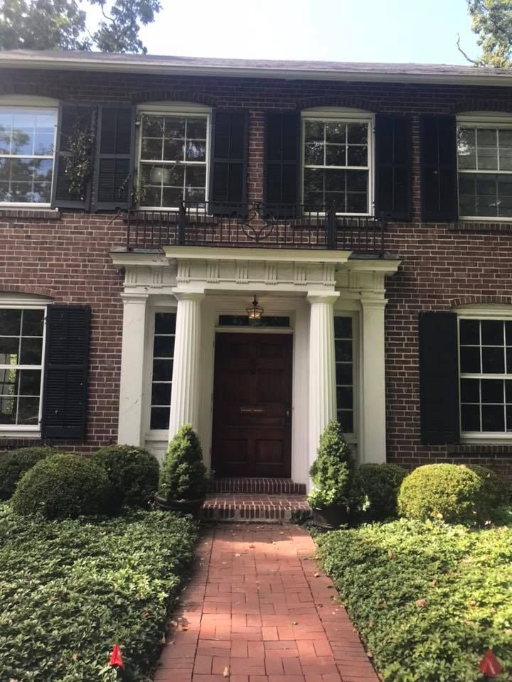 Brick house with white trim, black shutters, and red brick walkway leading to the front door.