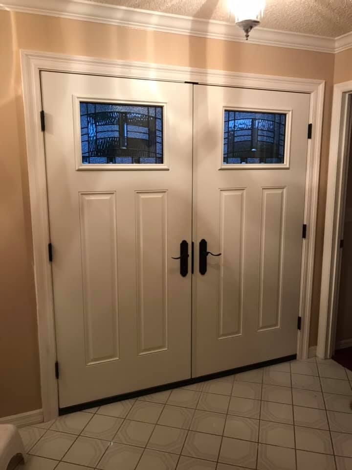 Double white doors with glass panels and black hardware in a tiled entryway.
