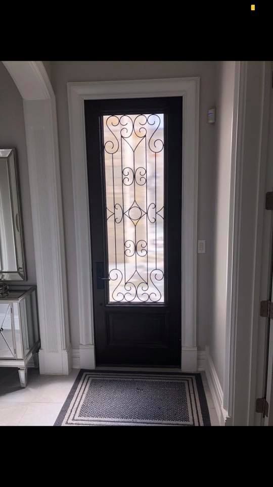 Black door with wrought iron design, glass panel, and gray entryway.