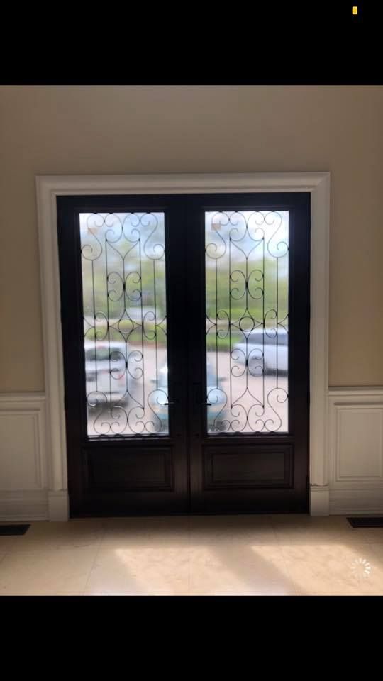 Dark wooden double doors with decorative glass panels; exterior view of cars and trees.