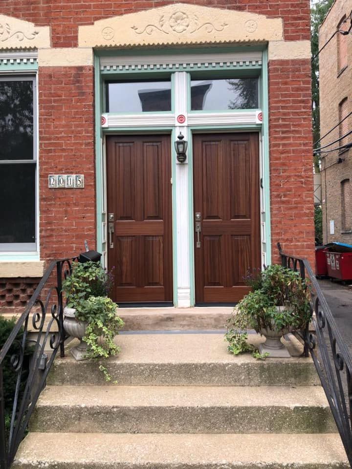 Two brown wooden doors with glass windows above, red brick building, concrete steps.