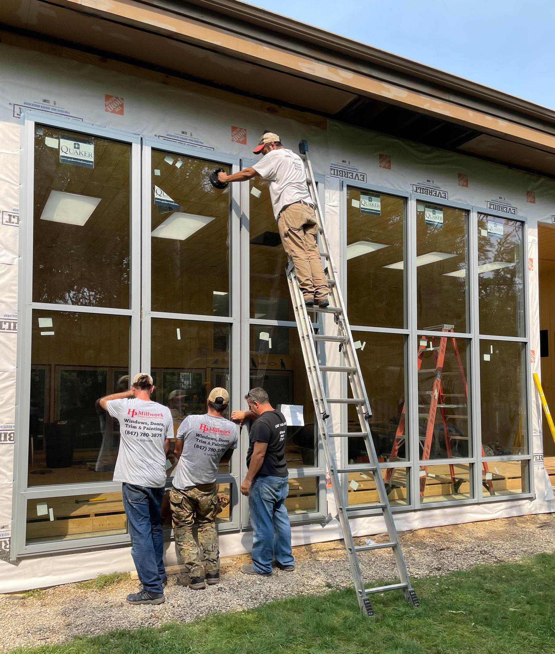 Construction workers installing a large window, one on a ladder. Exterior of a building under construction.