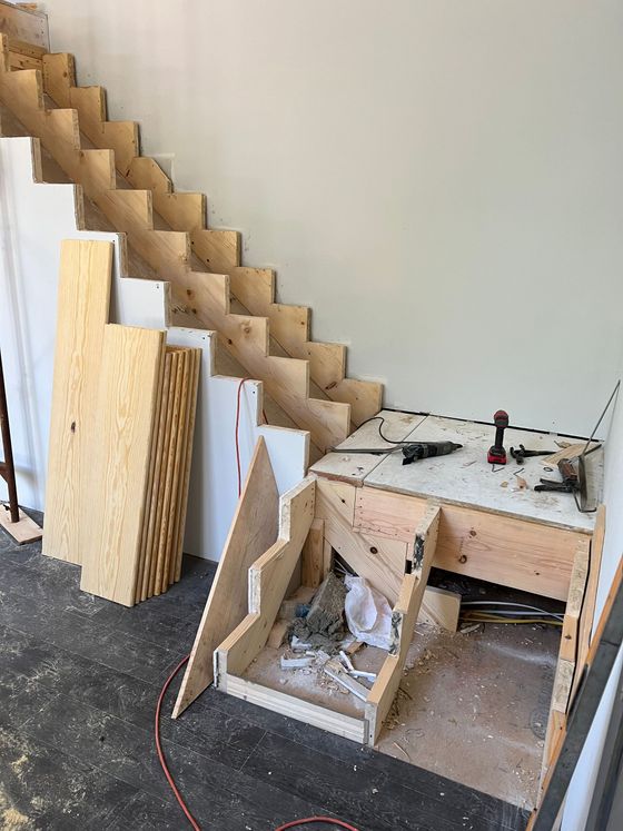 Unfinished wooden staircase under construction, featuring exposed stringers and a landing platform inside a room.