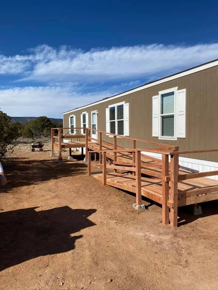 Long beige modular home with wooden ramps on a dirt lot under a blue sky