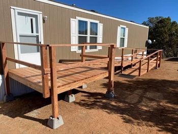Accessible wooden ramp and deck leading to a beige portable building with white doors and windows.
