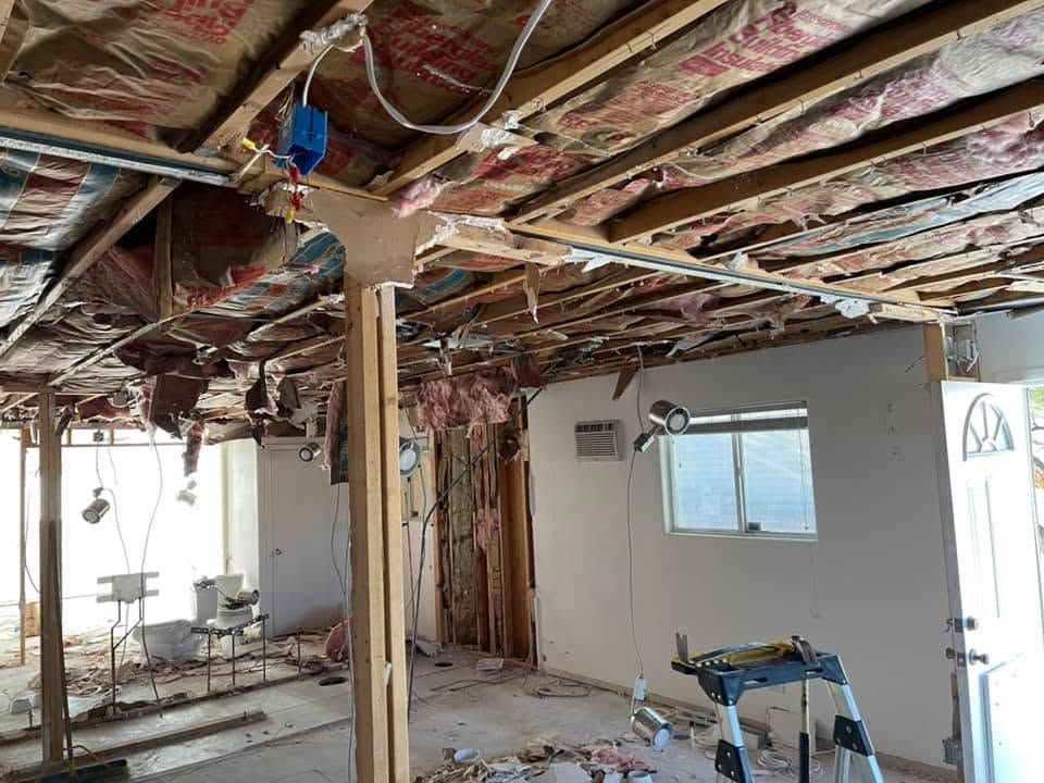 Interior room under renovation with exposed insulation, ceiling joists, tools, and debris on the floor