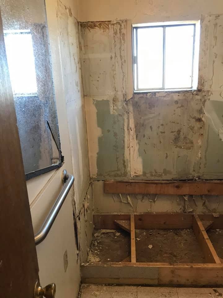 Deteriorated bathroom with peeling walls, exposed floor joists, and a window letting in light.