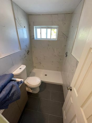 Small bathroom with a toilet, bathtub, dark tile floor, and a narrow window.
