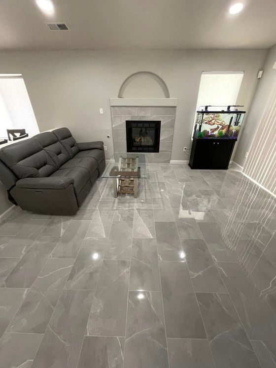 Modern living room with gray sofa, white fireplace, glossy tile floor, and fish tank cabinet on the right.