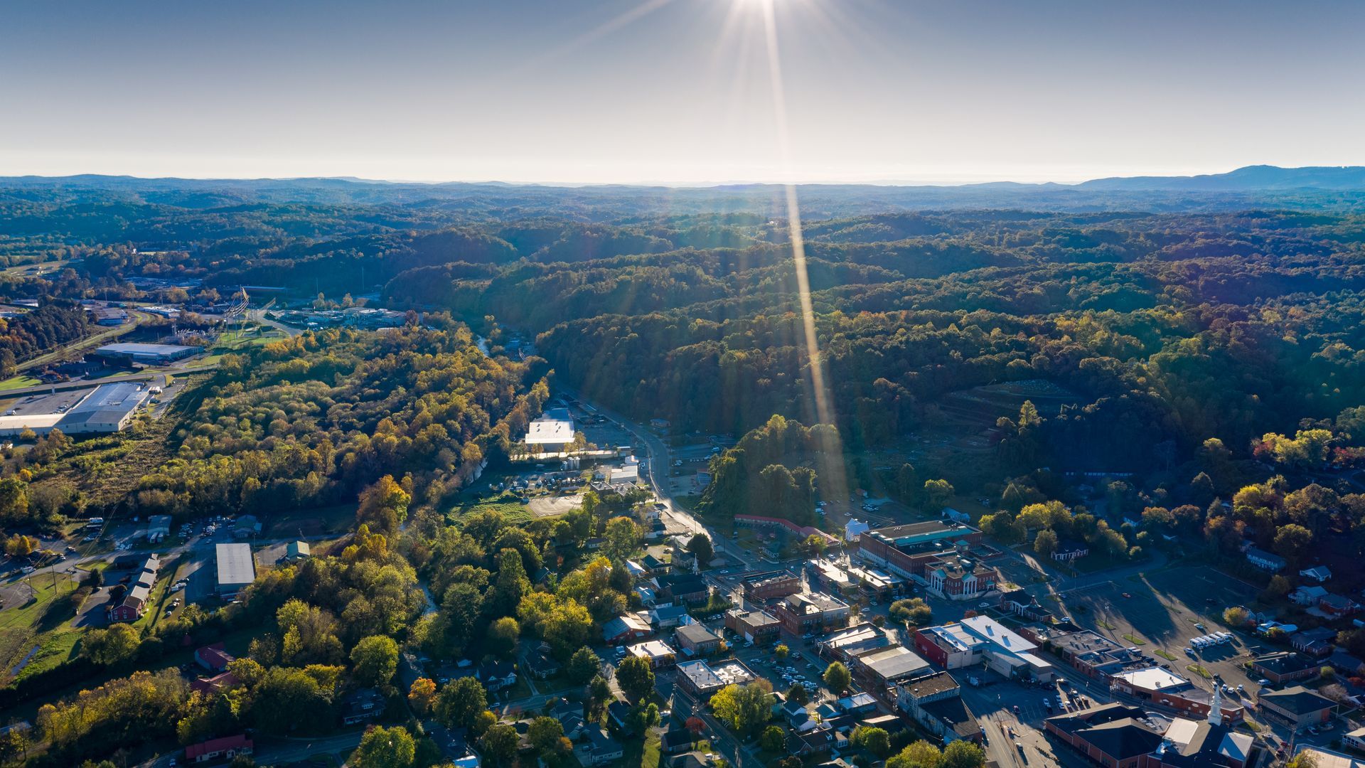 An aerial view of a small town in the mountains with the sun shining through the trees.