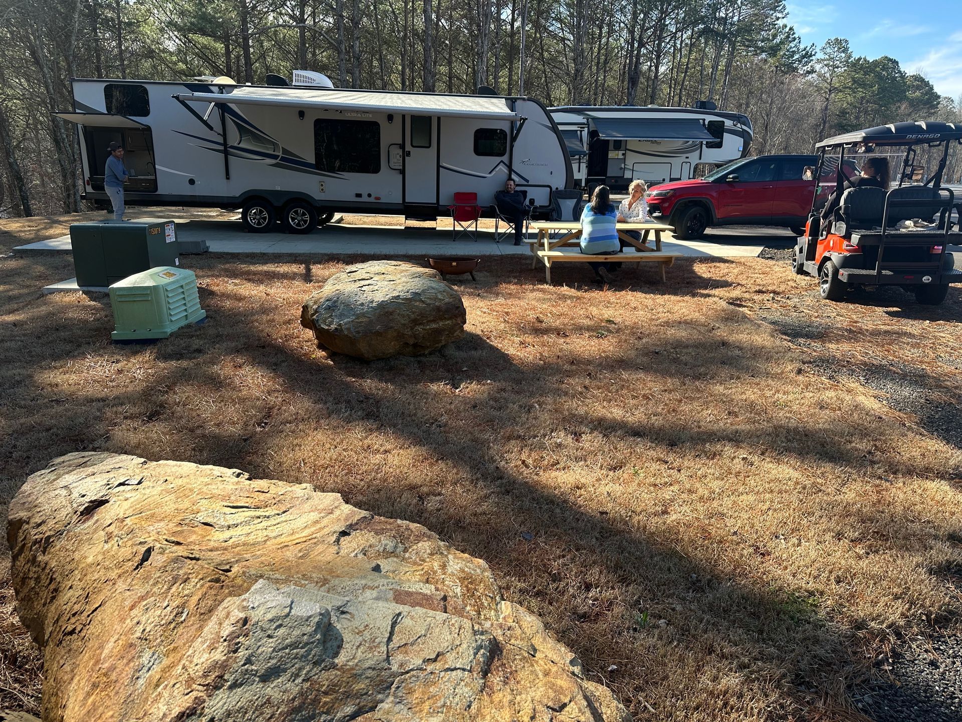 A group of people are sitting at a picnic table in front of a trailer.