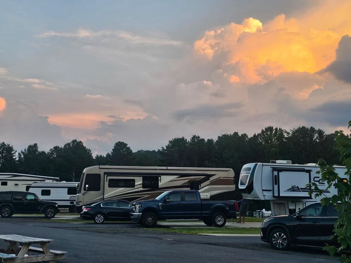 A group of rvs are parked in a park with picnic tables.