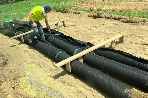 A man is laying a row of black pipes in the dirt.