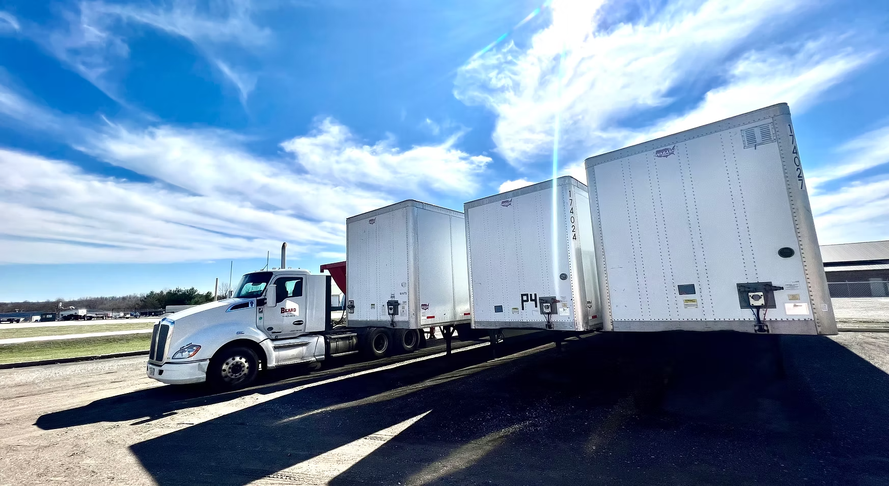 A white semi truck is parked next to a row of white boxes.