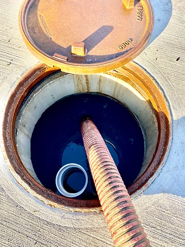 A manhole cover is open and a hose is coming out of it.
