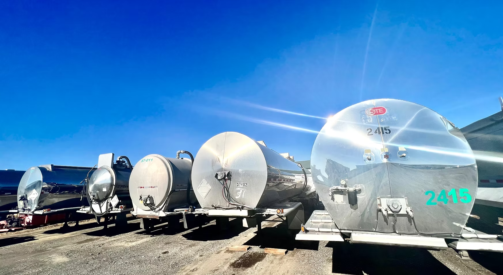 A row of tanker trucks are parked in a gravel lot.