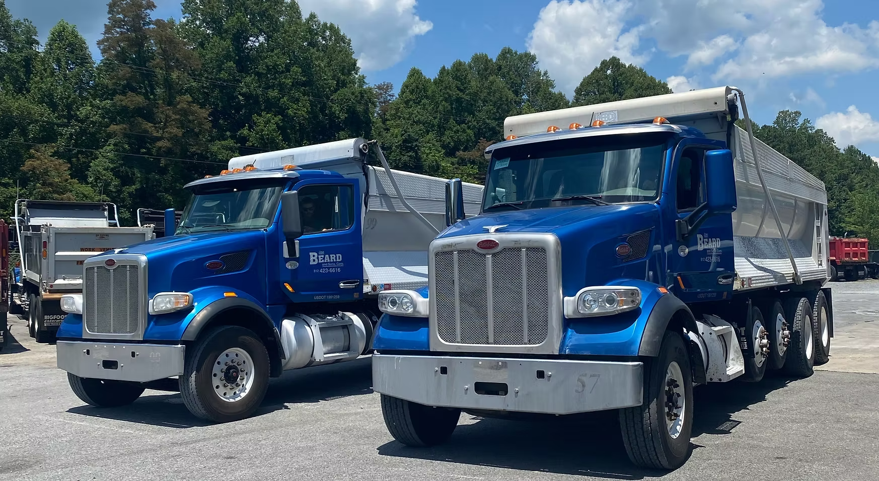 Two blue dump trucks are parked next to each other in a gravel lot.