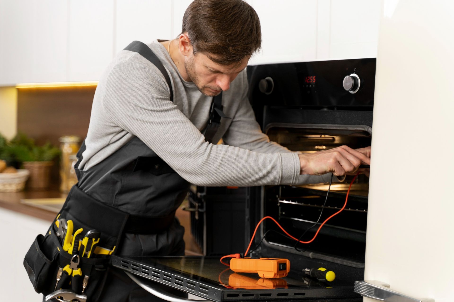 Electrician repairing an oven with a multimeter in a kitchen setting.