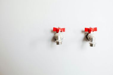 Two chrome faucets with red handles on a white wall.
