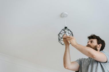 Man installs a black wire cage pendant light fixture on a white ceiling.