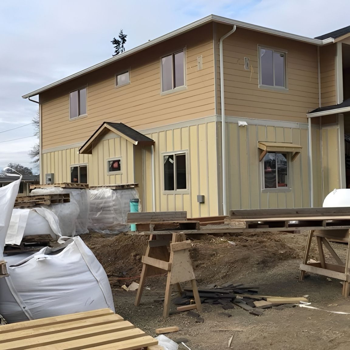 Two-story tan house under construction with scaffolding and building materials outside