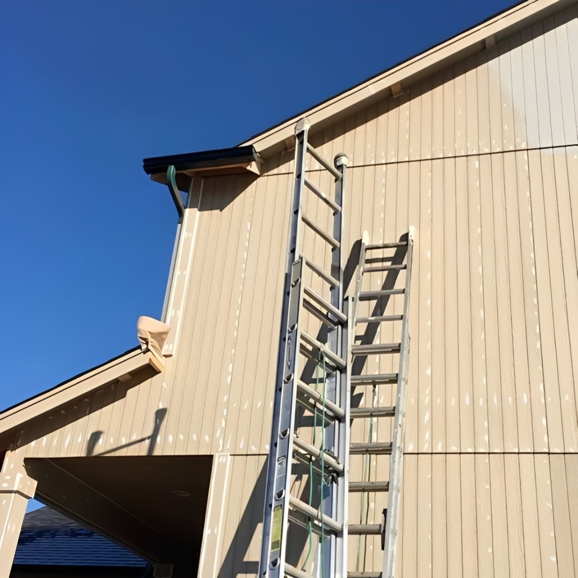 Two ladders leaning against a beige house under a blue sky