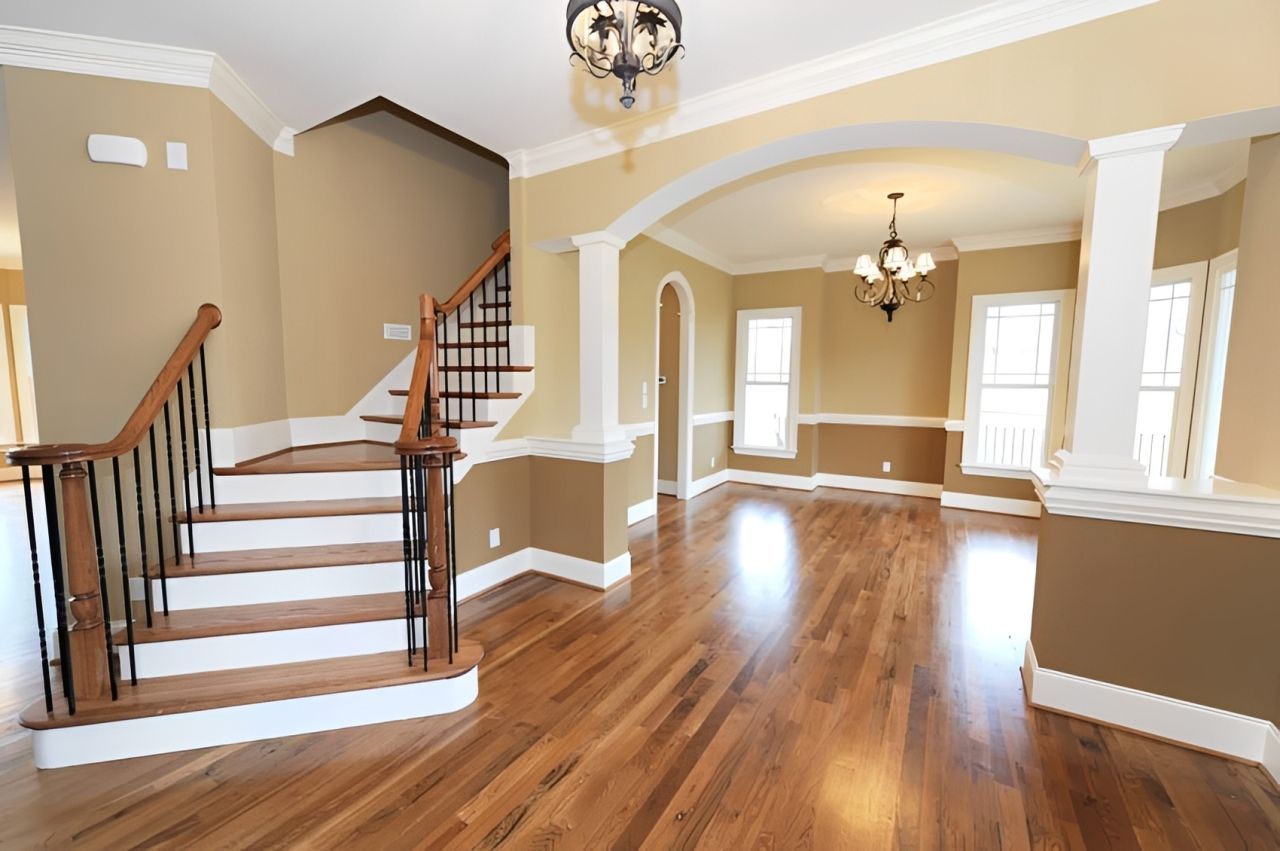 Spacious empty foyer with hardwood floors, curved staircase, and arched openings, painted beige and white.