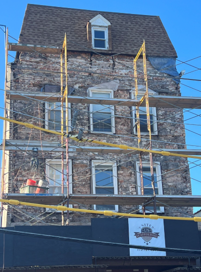 Scaffolded brick building under renovation behind a dark construction fence.