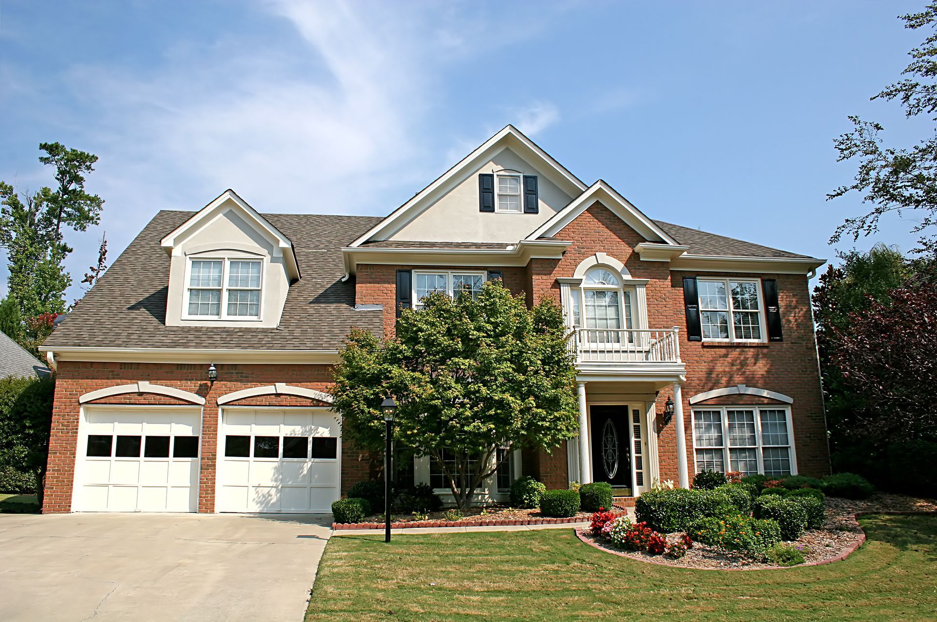 Large brick suburban house with white garage doors, gabled roof, and a front lawn in daylight