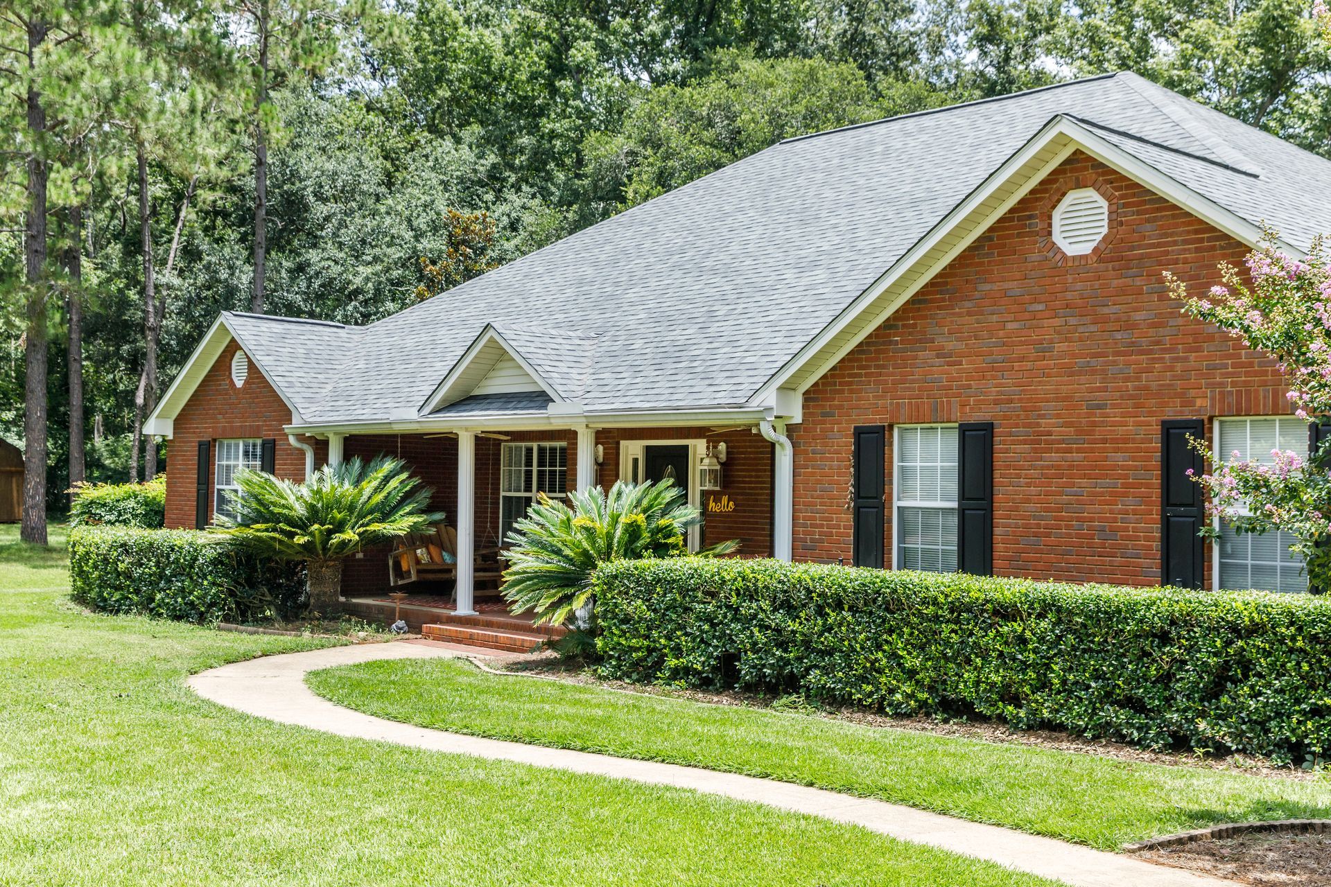 Brick house with white trim, front porch, and manicured lawn surrounded by trees