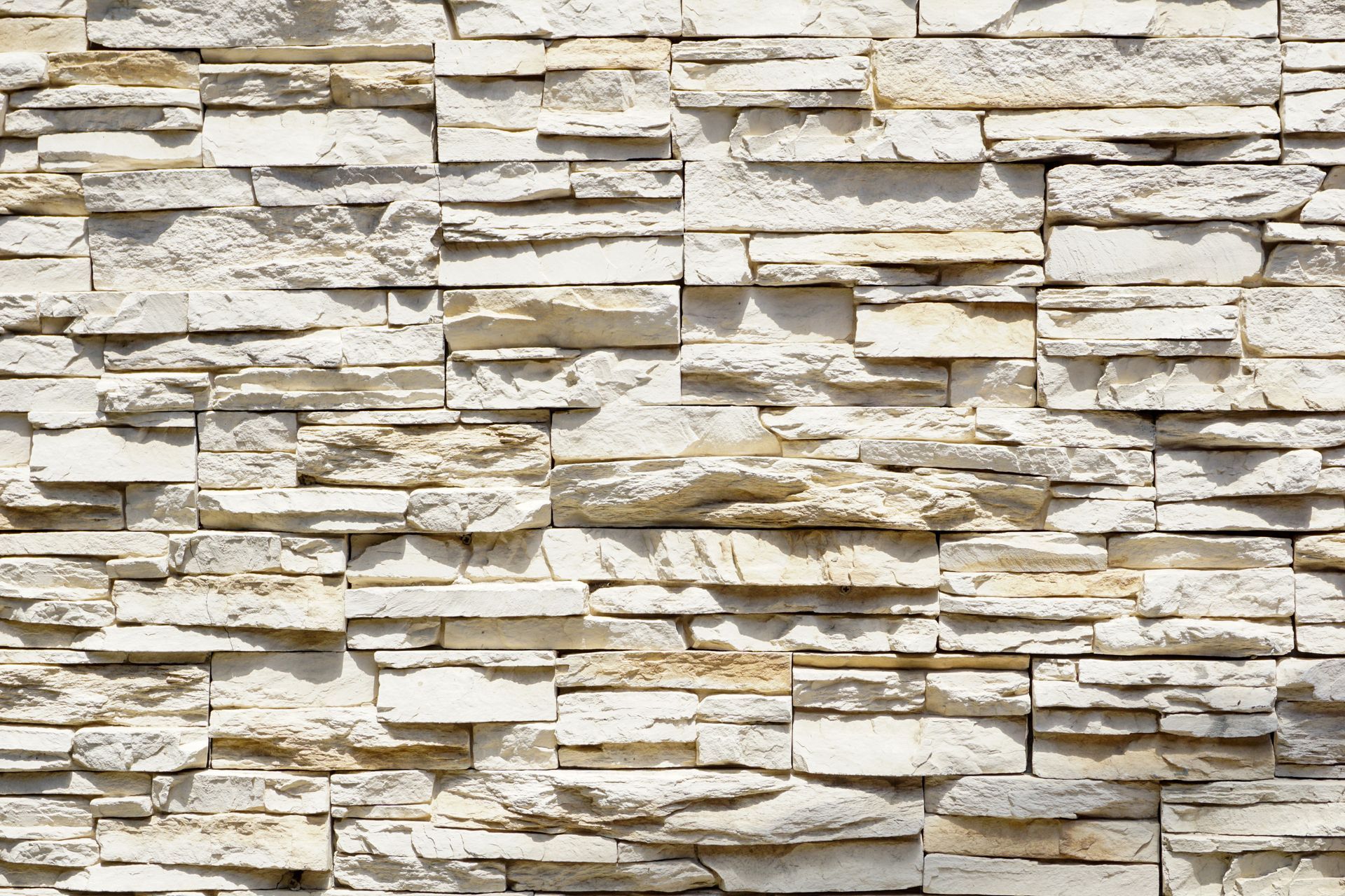 Close-up of a beige stacked stone wall with layered texture and light shadows