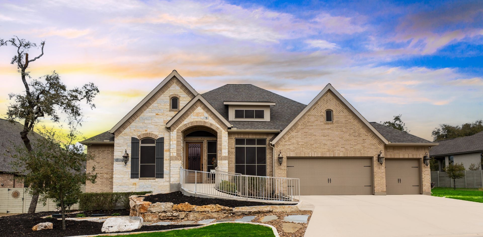 Single-story beige brick house with a three-car garage and landscaped front yard at sunset