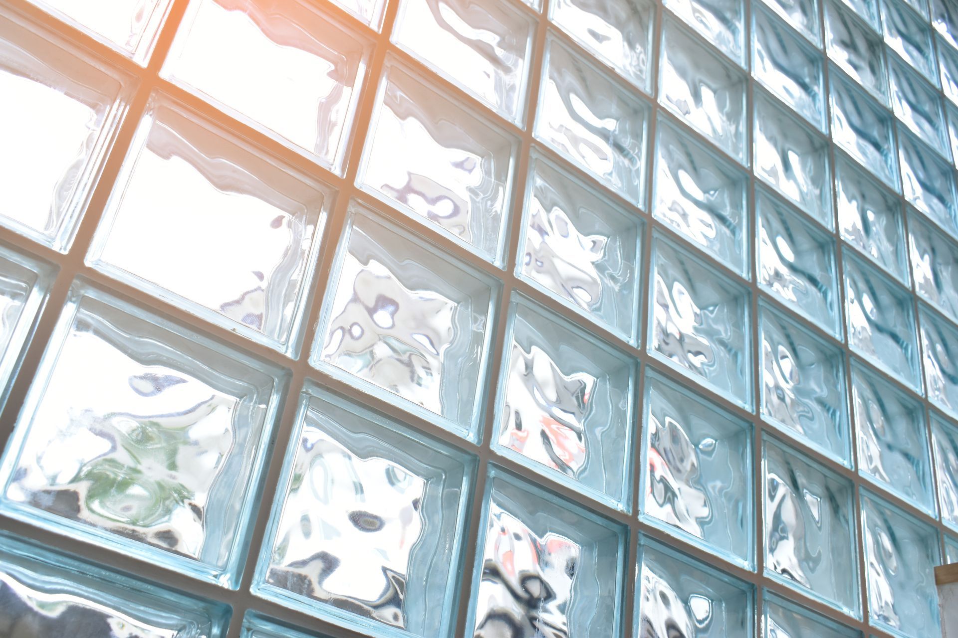 Sunlit frosted glass block wall with floral patterns and a warm orange reflection