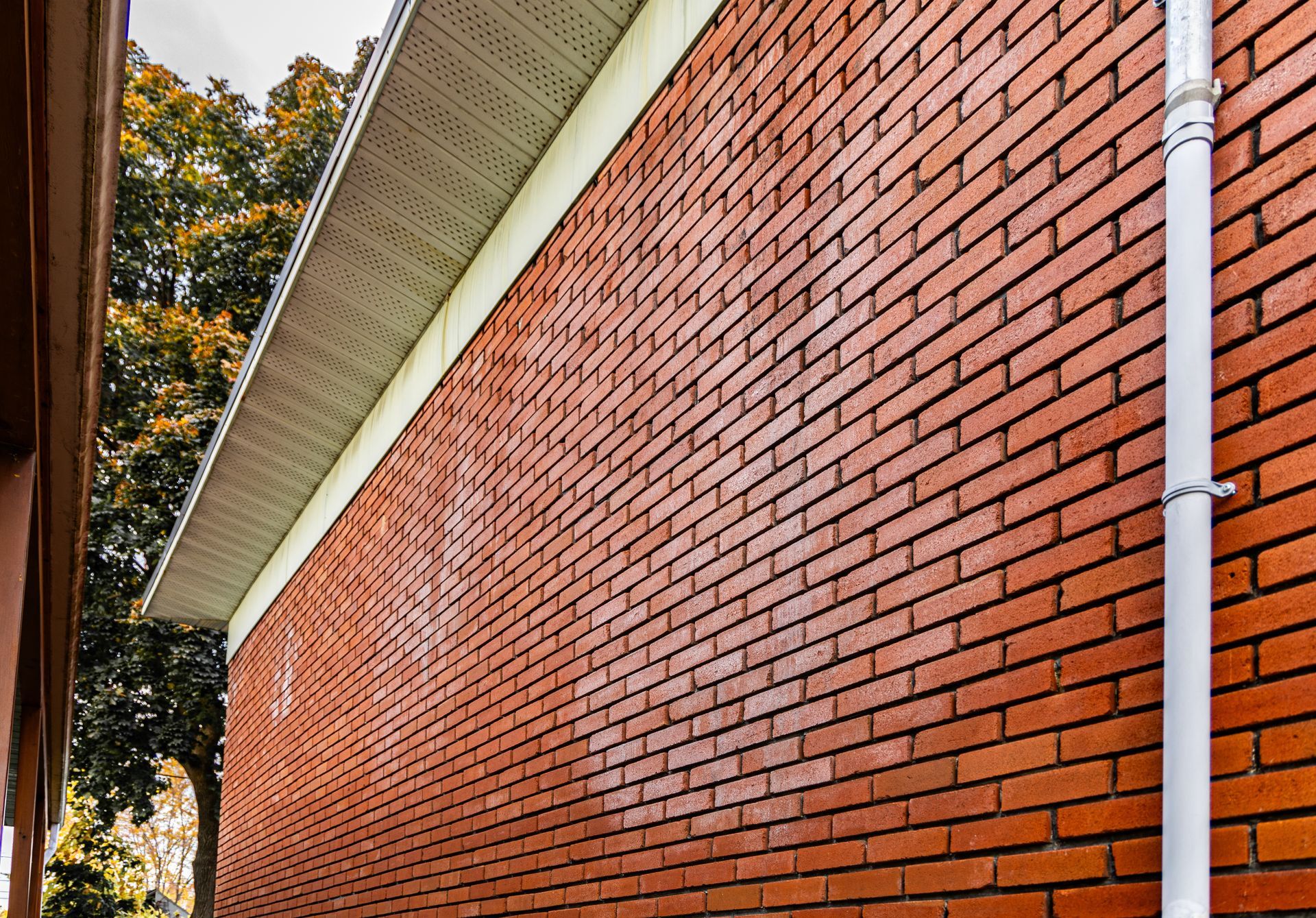 Red brick building wall with white trim and downspout under a slanted roofline